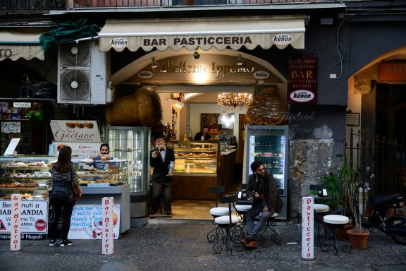 Entrada a una pastelería con mesas al aire libre y vitrinas de dulces.