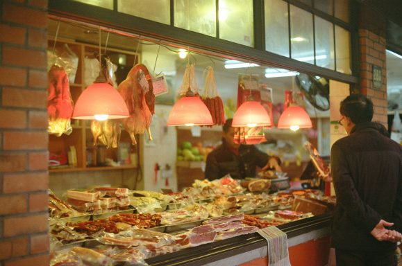 Carnicería con luces rojas y una persona mirando la variedad de carnes expuestas.