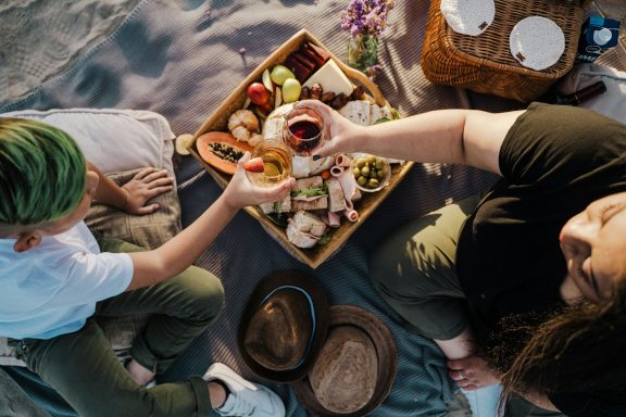 Pareja compartiendo comida en un picnic sobre una manta, con frutas y bocadillos.